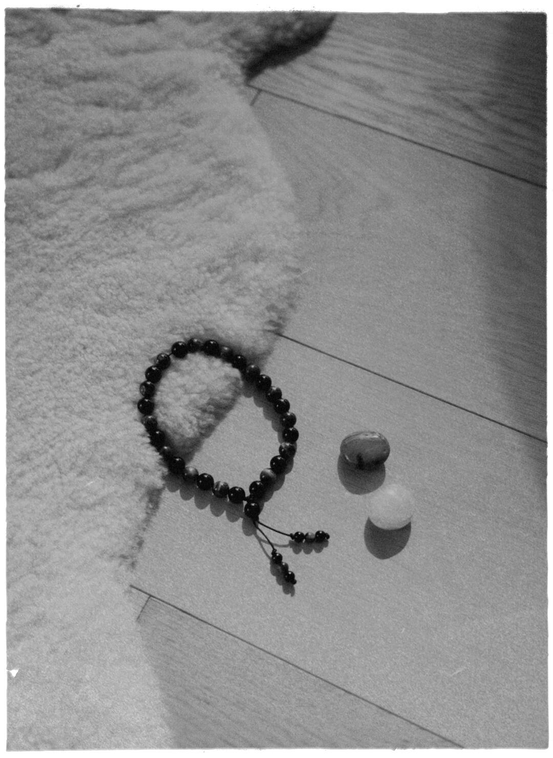 Mala beads and two stones on a sheepskin and a wooden floor, black and white